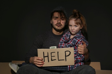 Poor father and daughter with HELP sign on floor near dark wall