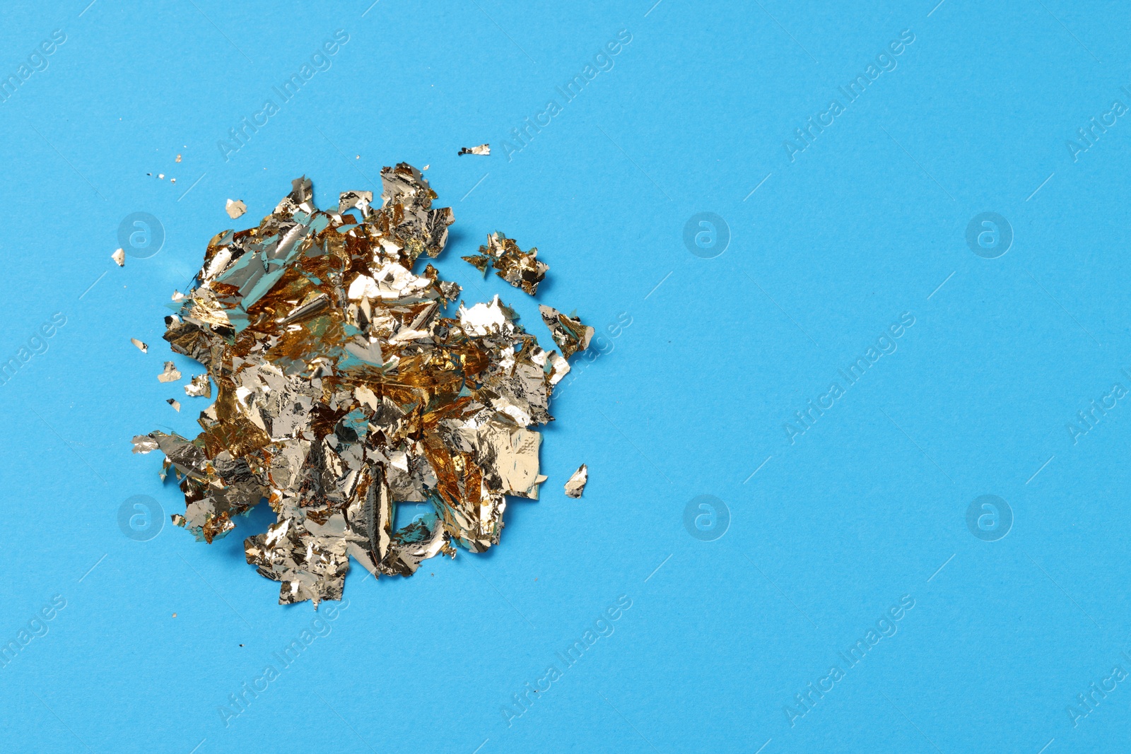 Photo of Pieces of edible gold leaf on light blue background, top view. Space for text