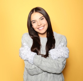 Image of Happy young woman wearing warm sweater and mittens on yellow background
