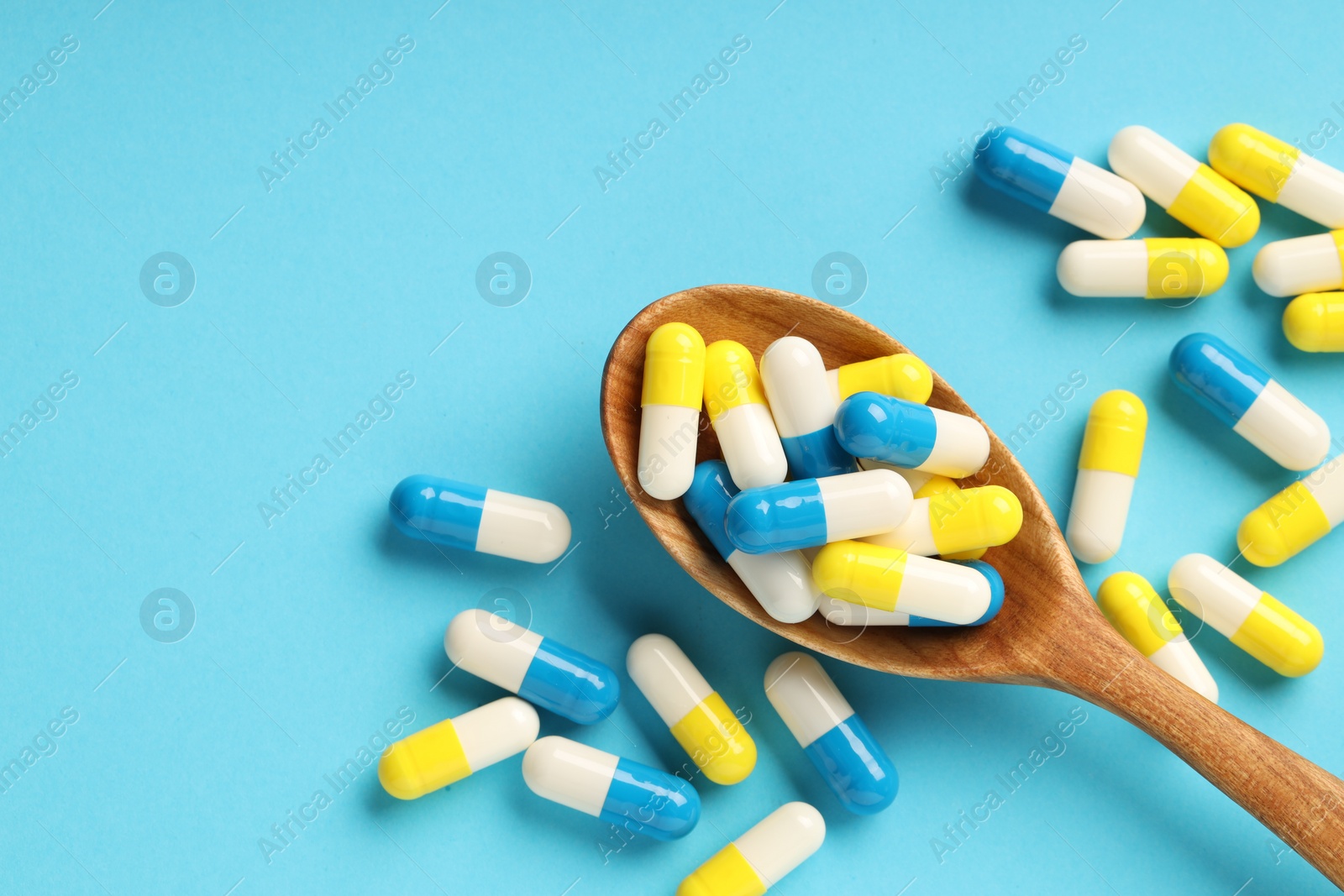 Photo of Many antibiotic pills with wooden spoon and space for text on light blue background, top view. Medicinal treatment