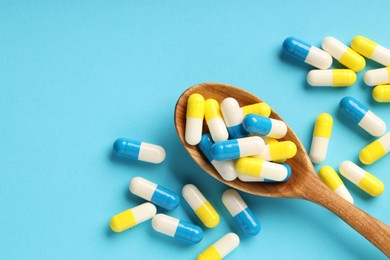 Many antibiotic pills with wooden spoon and space for text on light blue background, top view. Medicinal treatment