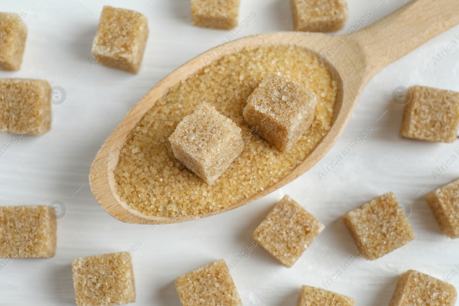 Photo of Brown sugar cubes in spoon on white wooden table, closeup