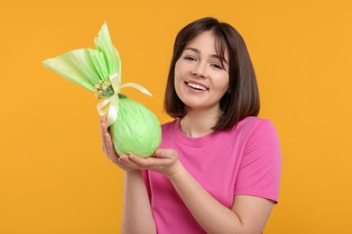 Photo of Easter celebration. Happy woman with wrapped egg on orange background
