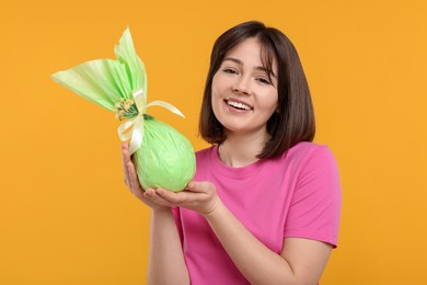 Easter celebration. Happy woman with wrapped egg on orange background