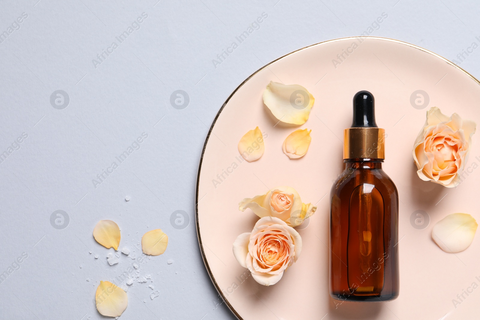 Photo of Bottle of cosmetic serum and beautiful flowers on light grey background, flat lay. Space for text