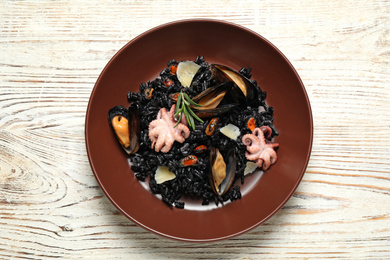 Photo of Delicious black risotto with seafood on white wooden table, top view