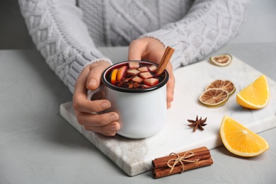 Photo of Woman holding mug with hot mulled wine on table, closeup