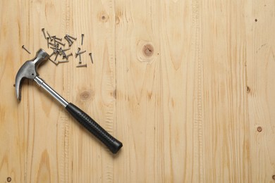 Photo of New hammer and metal nails on wooden table, flat lay. Space for text