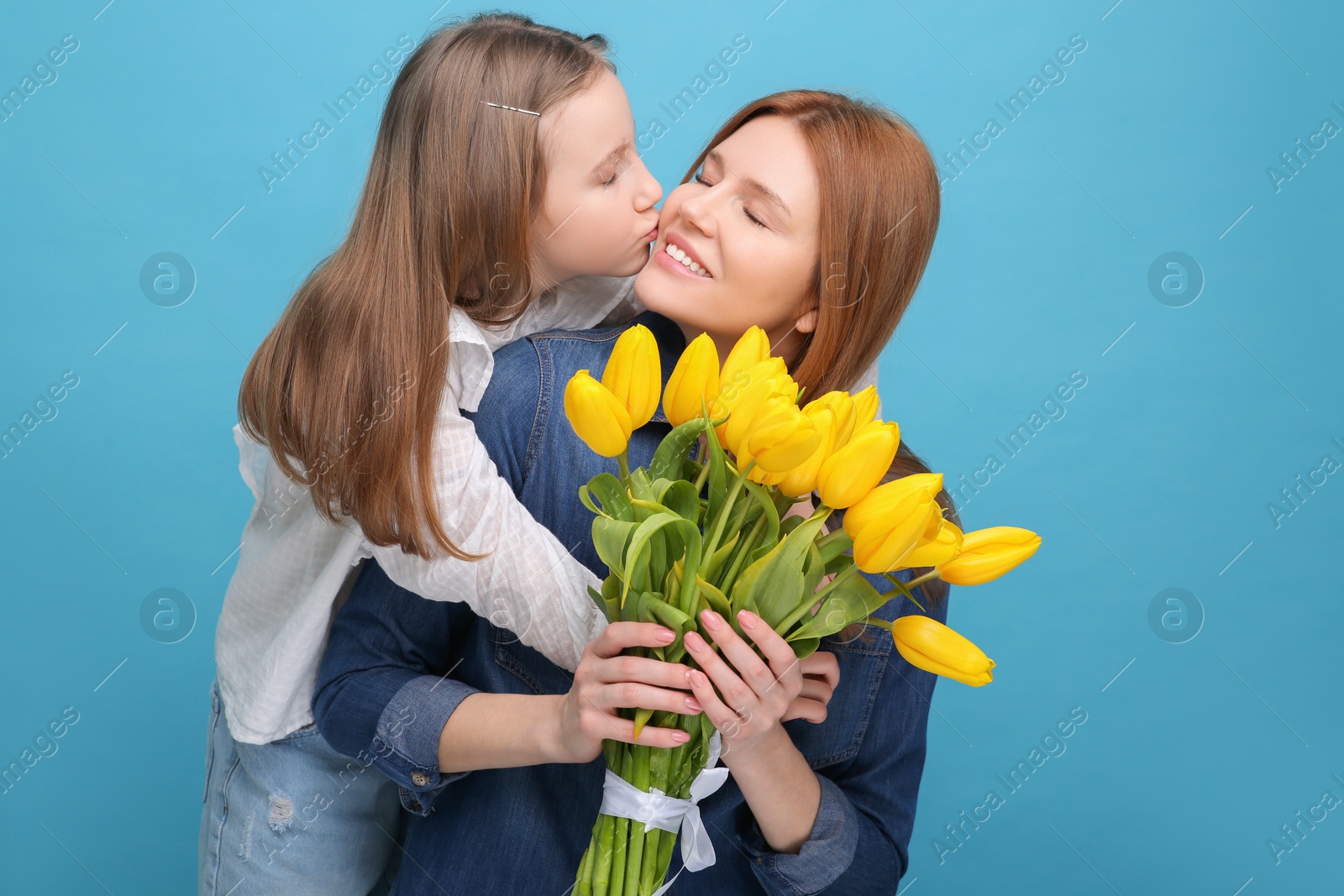 Photo of Mother and her cute daughter with bouquet of yellow tulips on light blue background