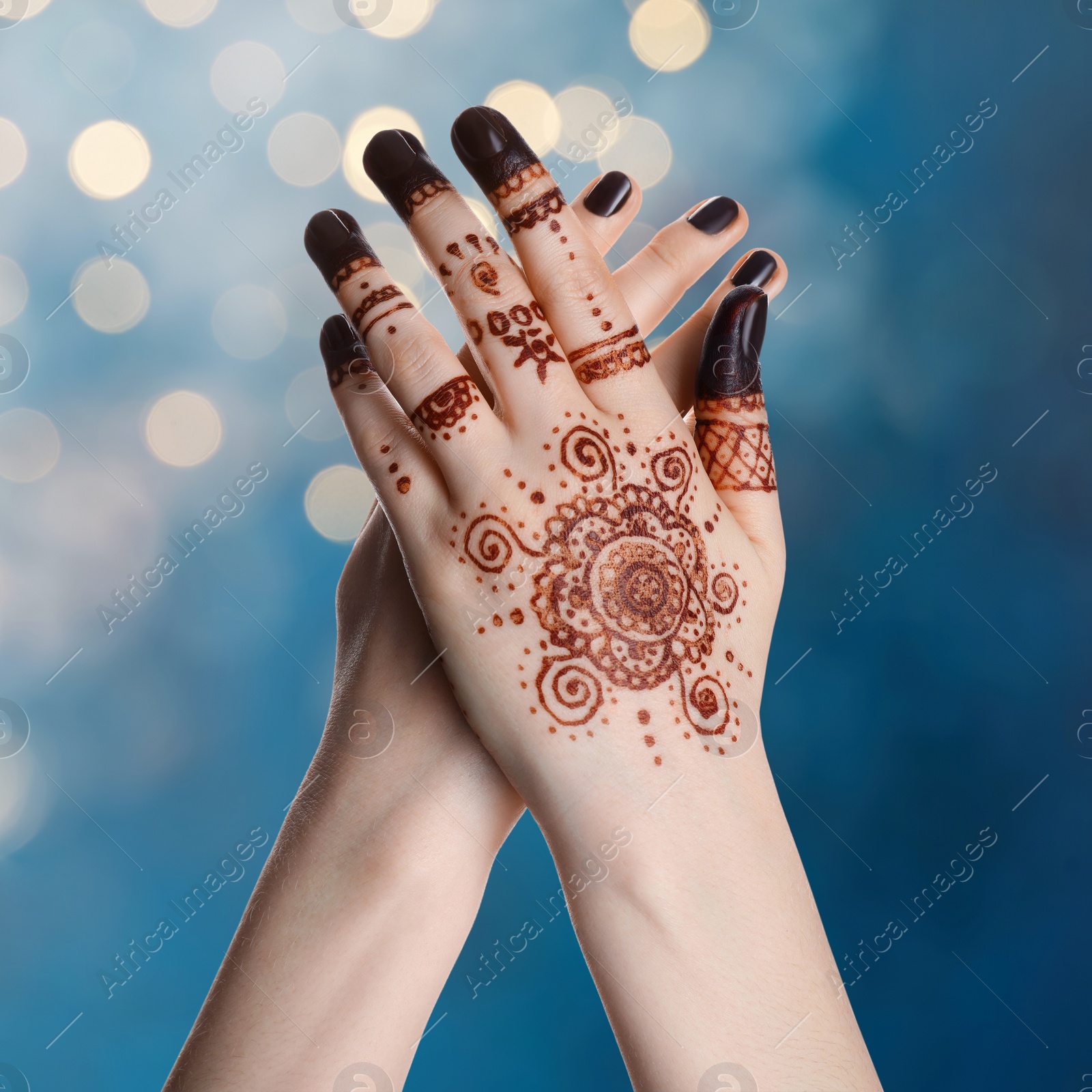 Image of Woman with henna tattoo on hand against blurred lights, bokeh effect