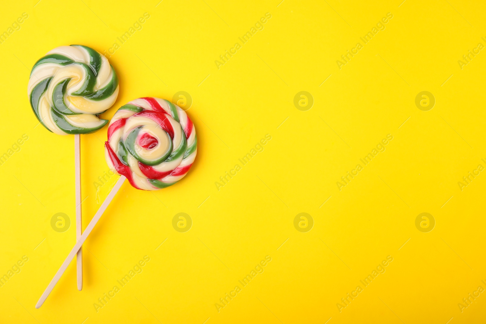 Photo of Colorful lollipops on yellow background, flat lay. Space for text