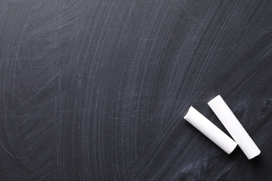 Photo of Pieces of white chalk on blackboard, flat lay. Space for text