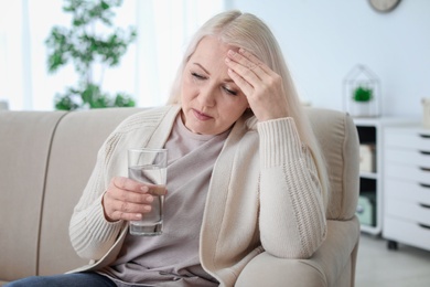 Photo of Mature woman with medicine in glass against headaches on sofa at home