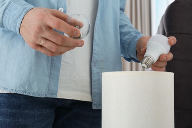 Photo of Man changing light bulb in lamp indoors, closeup