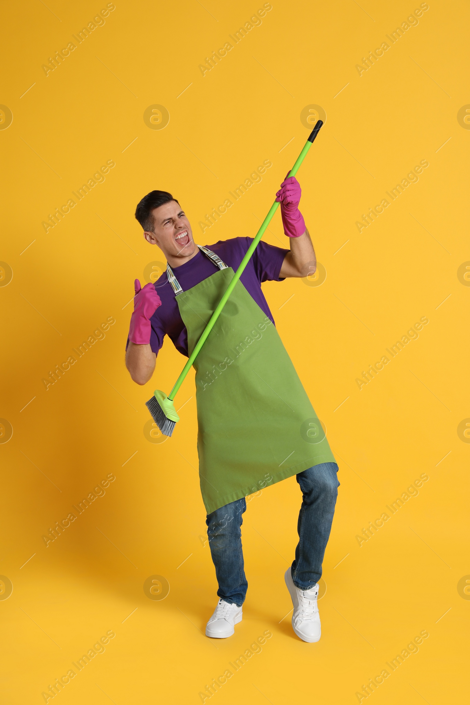 Photo of Man with green broom having fun on orange background