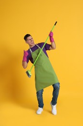 Photo of Man with green broom having fun on orange background