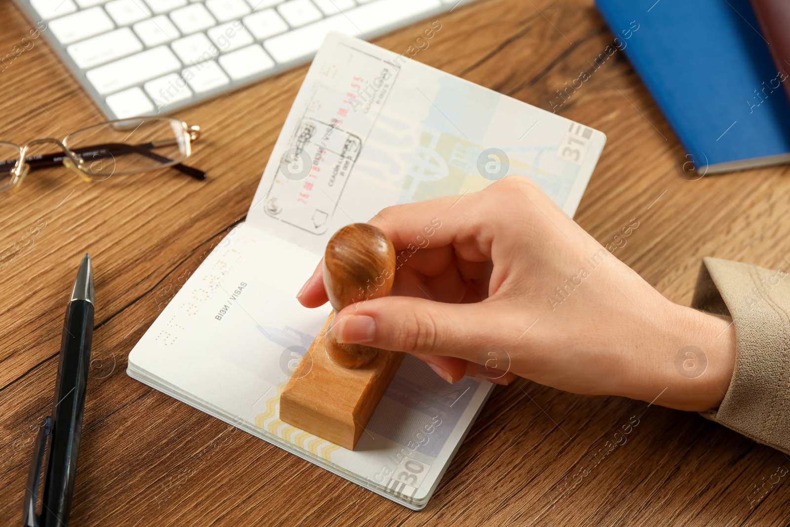 Photo of Moldova, Ceadir-Lunga - June 13, 2022: Woman stamping visa page in passport at wooden table, closeup