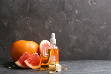 Photo of Bottles of essential oil and grapefruits on grey table, space for text