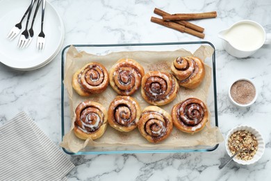 Tasty cinnamon rolls served on white marble table, flat lay