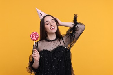 Photo of Happy woman in party hat holding lollipop on orange background