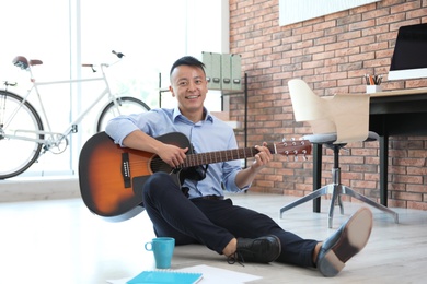 Photo of Happy young businessman playing guitar during break in office. Peaceful moment