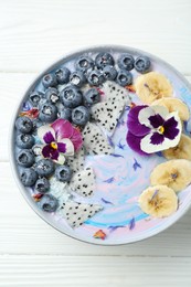 Photo of Delicious smoothie bowl with fresh fruits, blueberries and flowers on white wooden table, top view