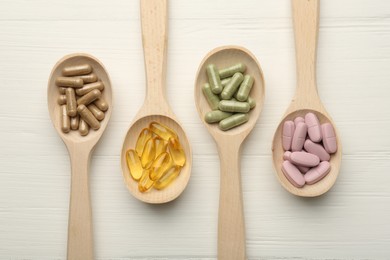 Photo of Different vitamin capsules in spoons on white wooden table, flat lay