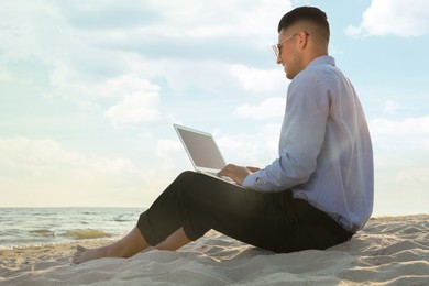 Photo of Businessman working with laptop on beach. Business trip