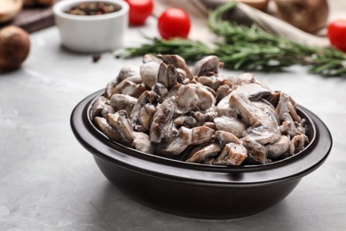 Photo of Bowl with delicious cooked mushrooms on grey table