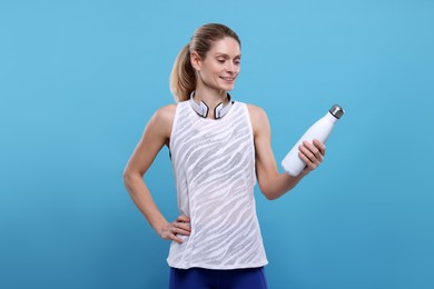 Photo of Sportswoman with thermo bottle and headphones on light blue background, space for text
