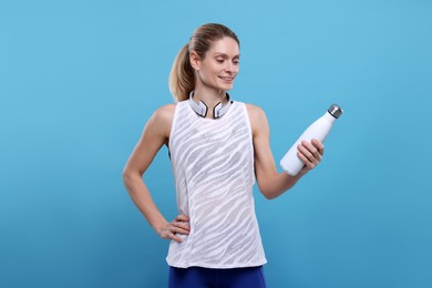 Sportswoman with thermo bottle and headphones on light blue background, space for text