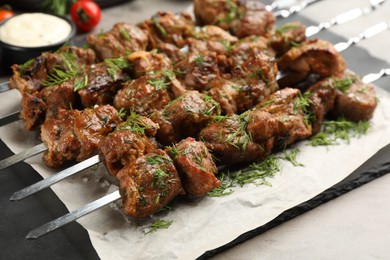 Metal skewers with delicious meat served on light grey table, closeup