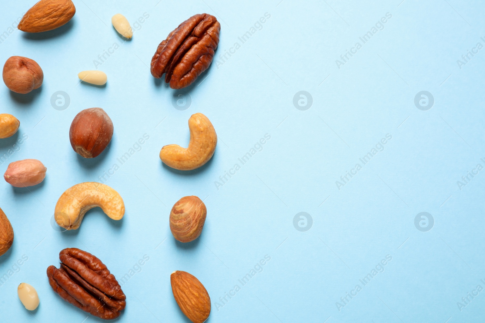 Photo of Different delicious nuts on light blue background, flat lay. Space for text