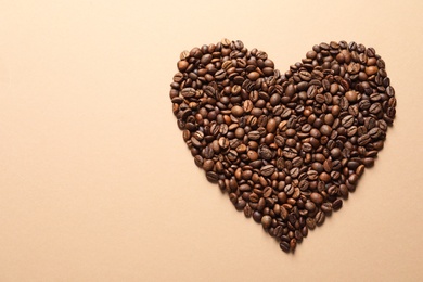 Heart shaped pile of coffee beans on light orange background, top view with space for text