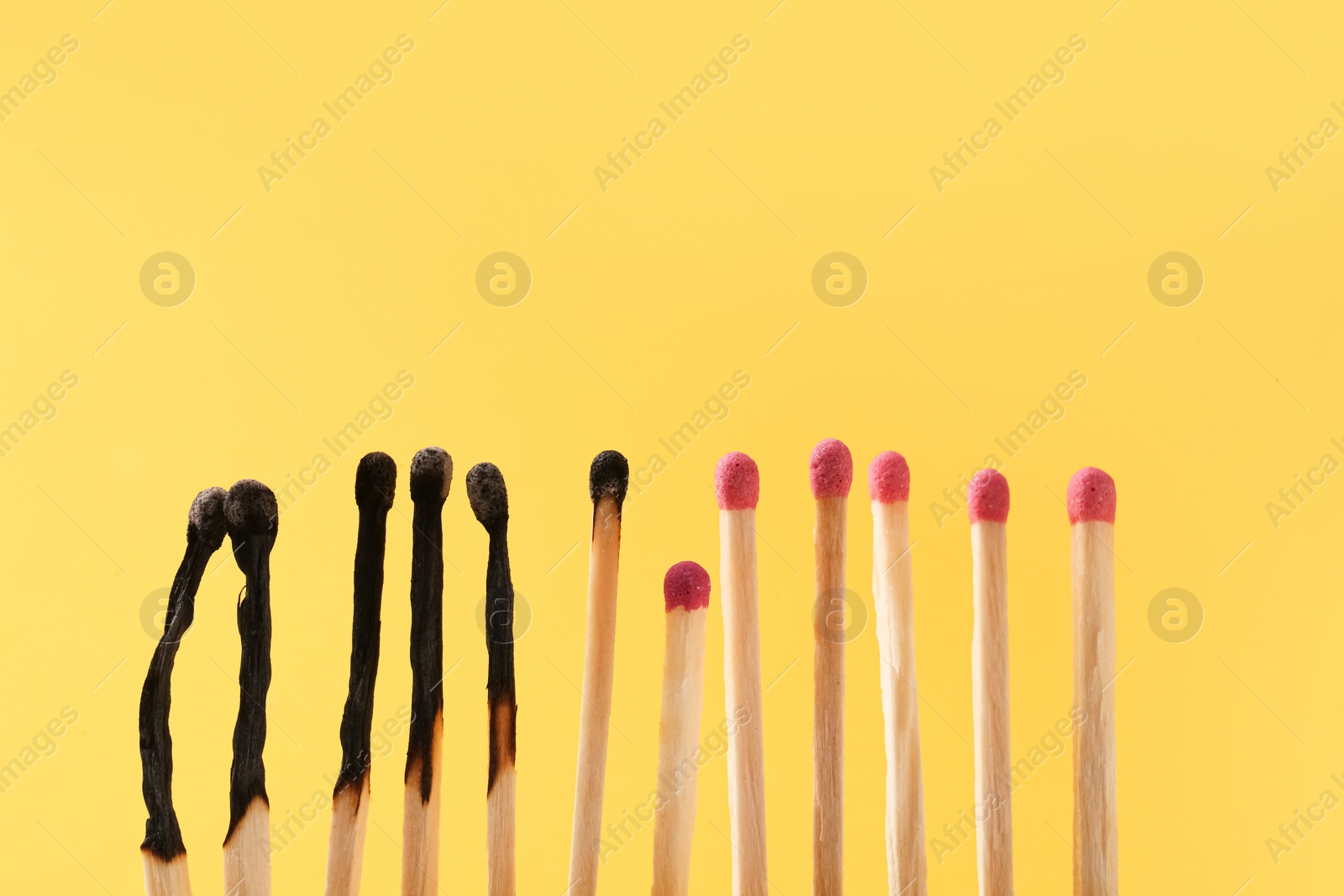 Photo of Burnt and whole matches on yellow background. Space for text