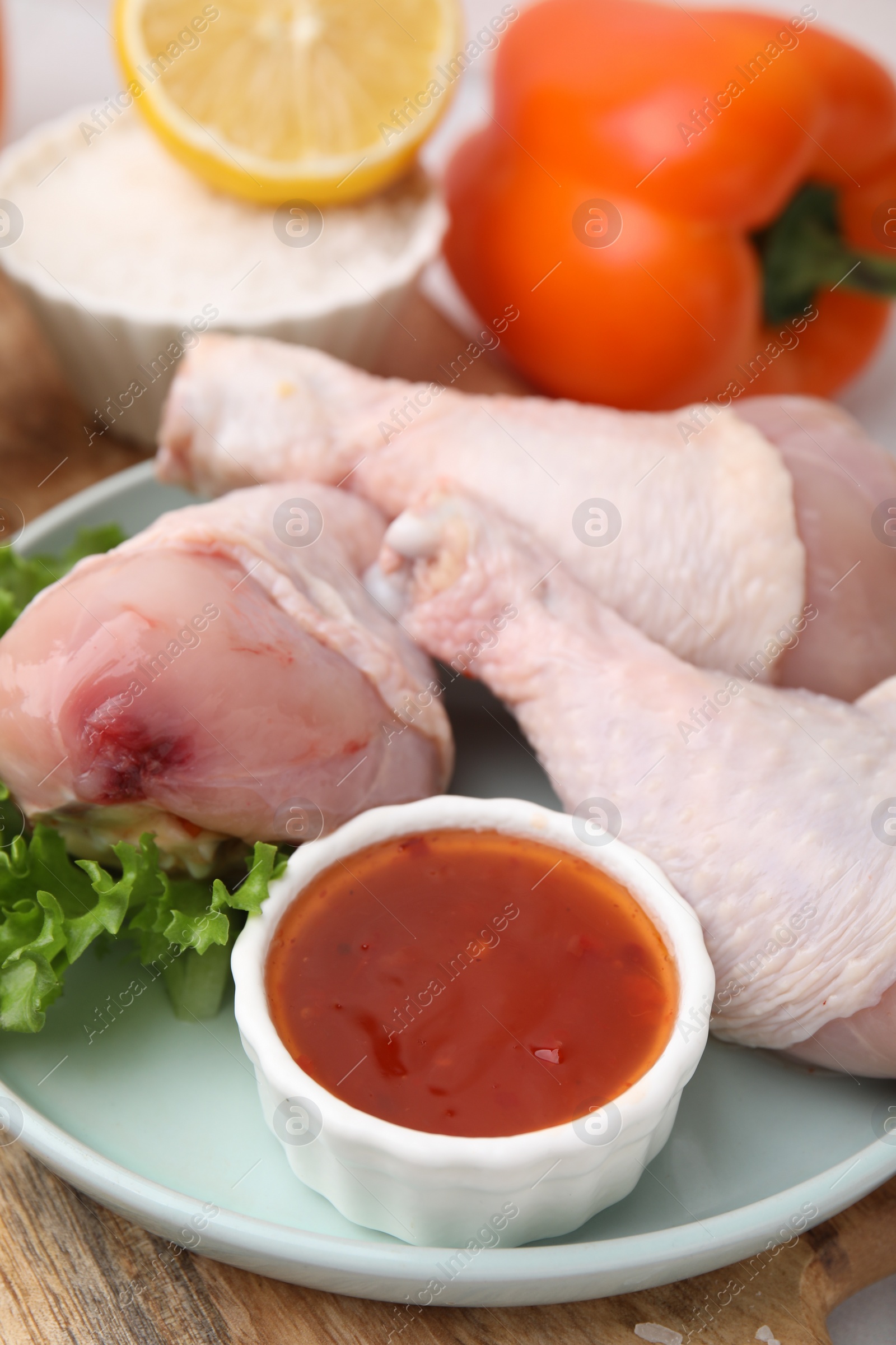 Photo of Fresh marinade, raw chicken drumsticks and lettuce on table, closeup