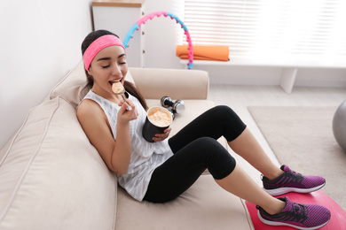 Photo of Lazy young woman eating ice cream instead of training at home