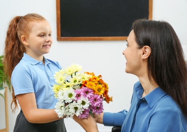 Photo of Schoolgirl congratulating her pedagogue with bouquet in classroom. Teacher's day