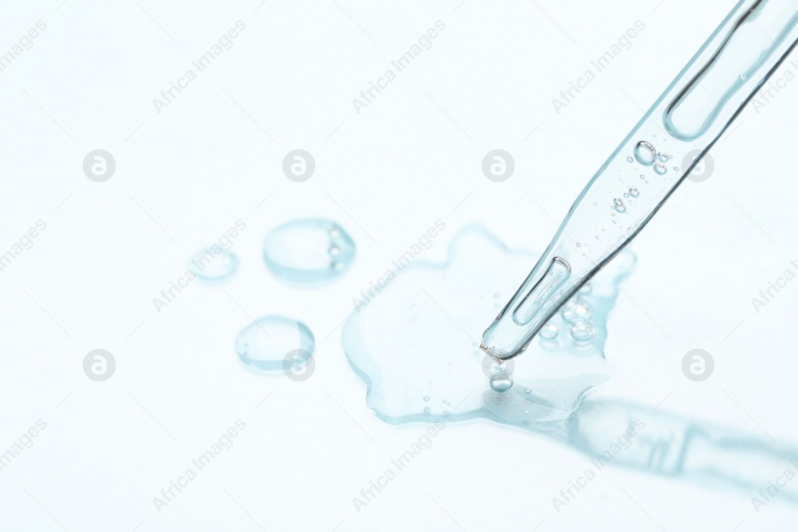 Photo of Glass pipette and transparent liquid on light background, closeup. Space for text