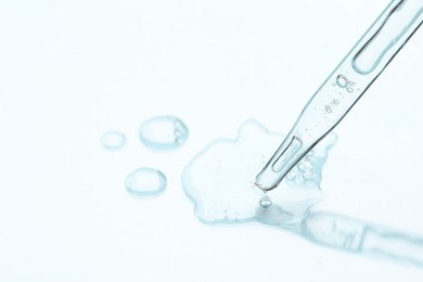 Photo of Glass pipette and transparent liquid on light background, closeup. Space for text