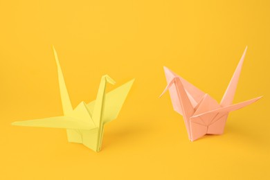 Photo of Origami art. Beautiful pale pink and light yellow paper cranes on orange background