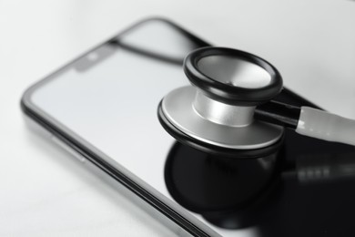 Photo of Modern smartphone and stethoscope on white table, closeup