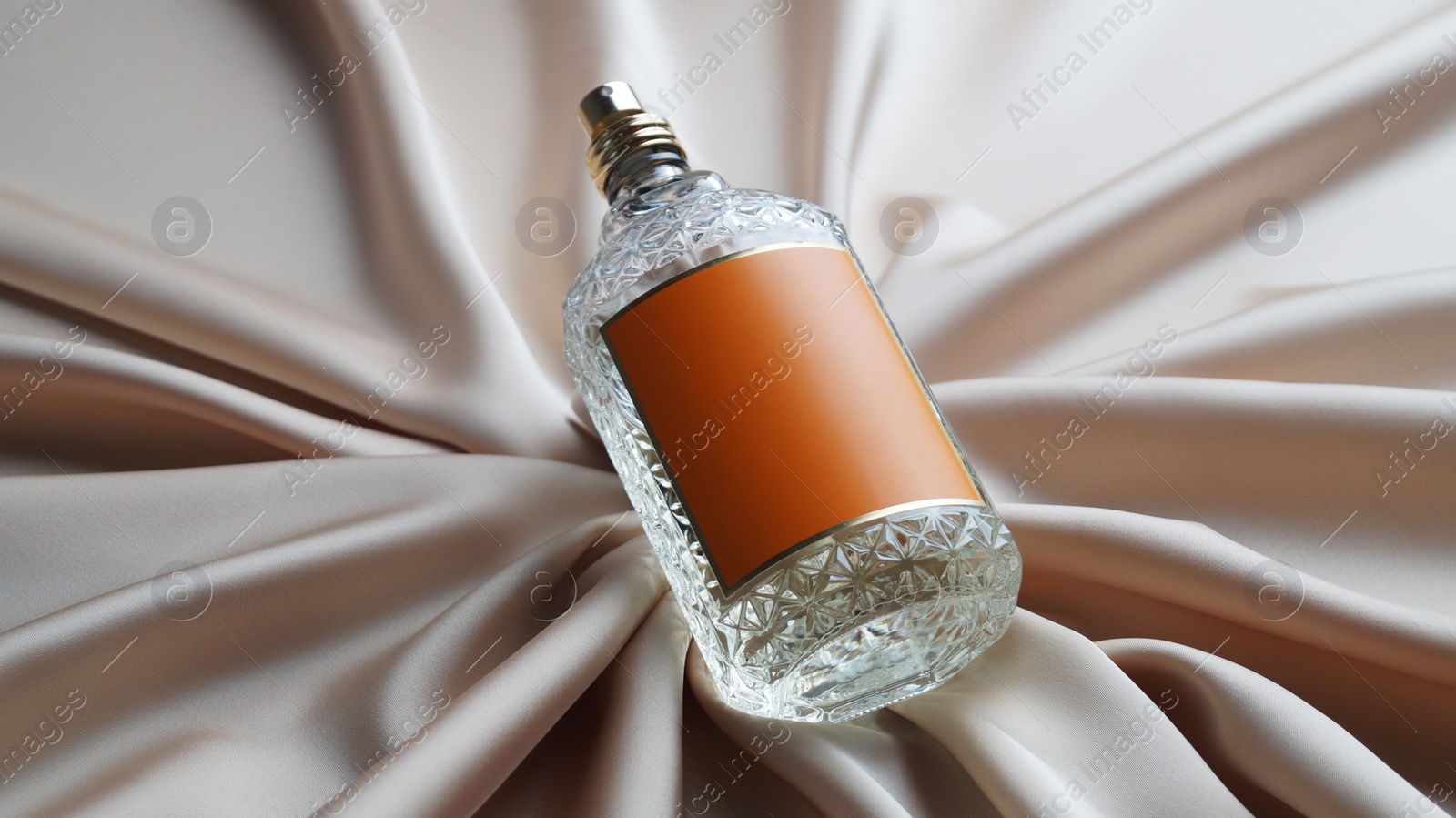 Photo of Luxury bottle of perfume on beige silk, closeup