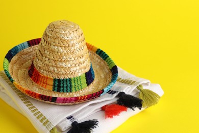 Photo of Mexican sombrero hat and poncho on yellow background, space for text