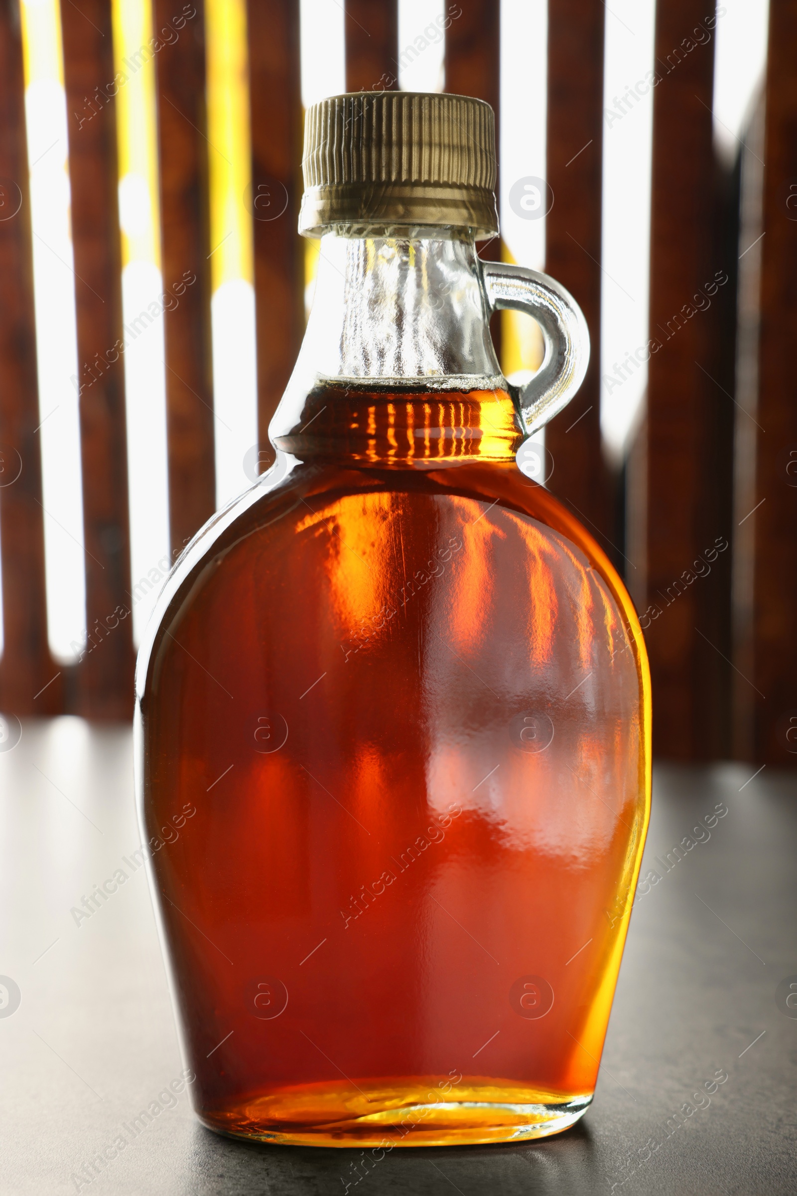 Photo of Bottle of tasty maple syrup on grey table