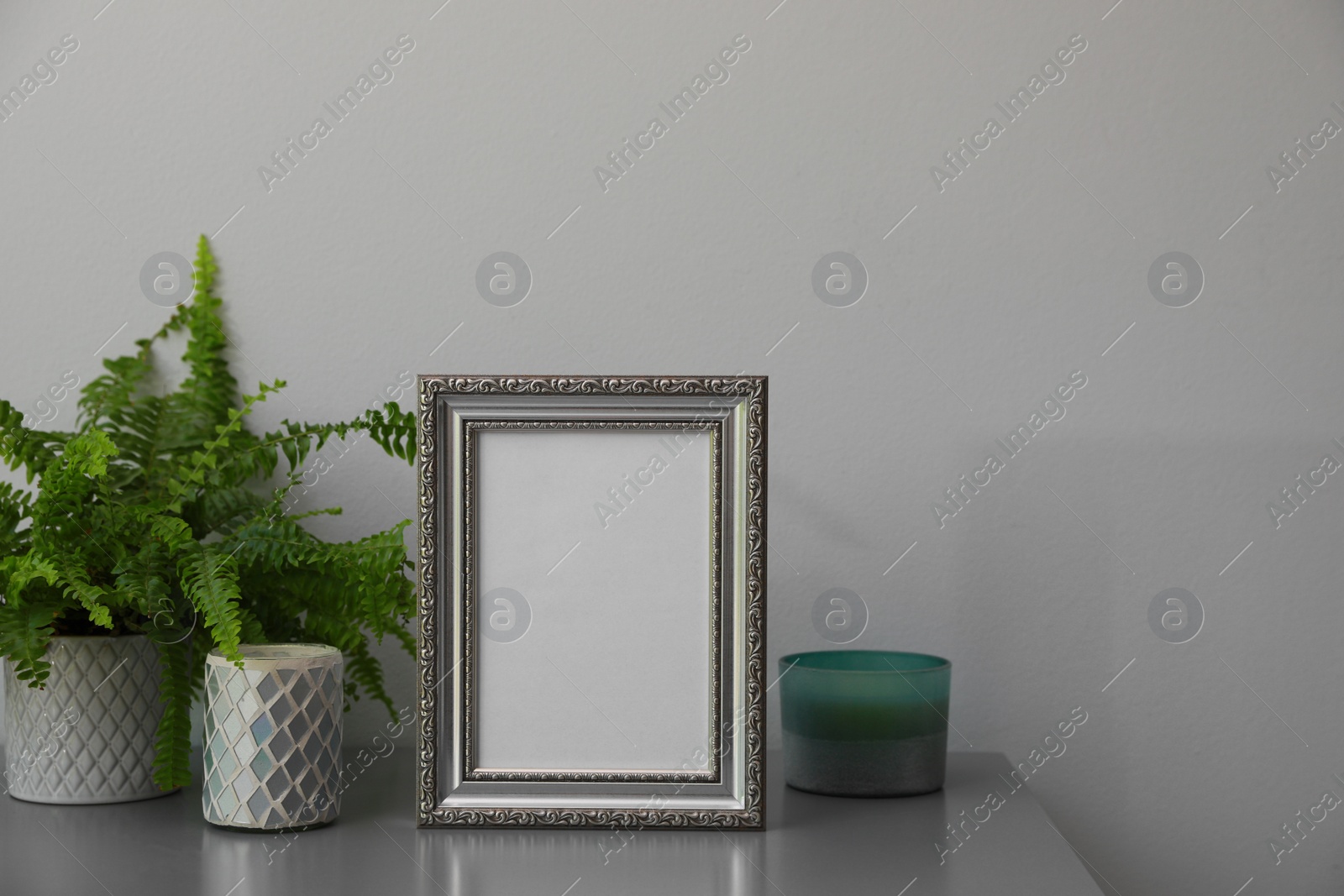 Photo of Empty photo frame, candles and green plant on grey table