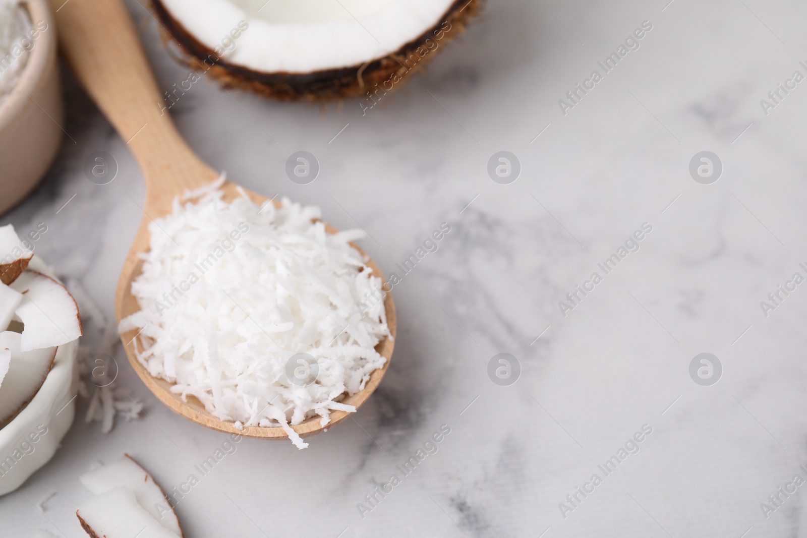 Photo of Coconut flakes in wooden spoon on white marble table, closeup. Space for text