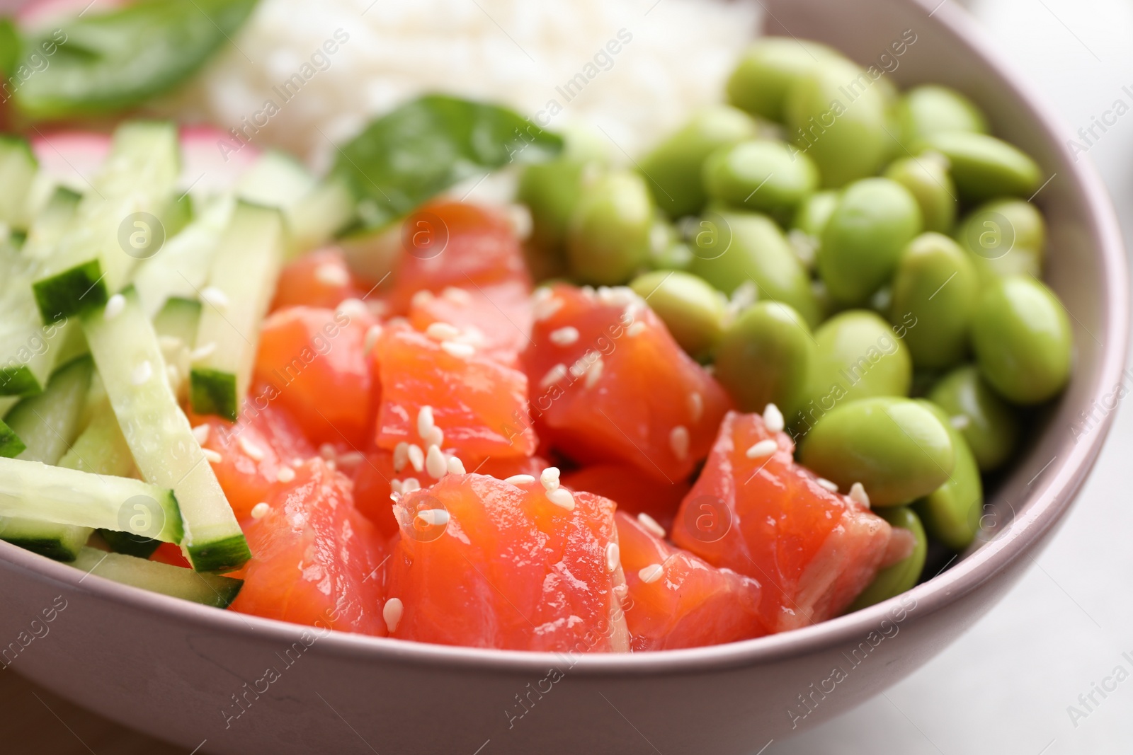 Photo of Poke bowl with salmon, edamame beans and vegetables on light grey table, closeup