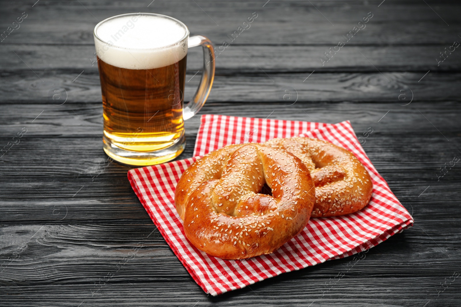 Photo of Tasty pretzels and glass of beer on black wooden table