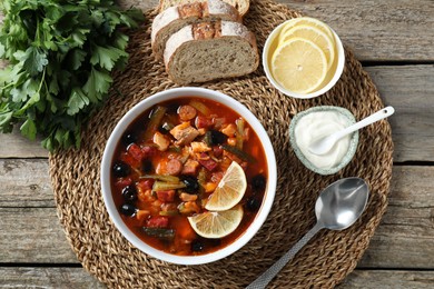 Meat solyanka soup with sausages, olives and vegetables served on wooden table, flat lay